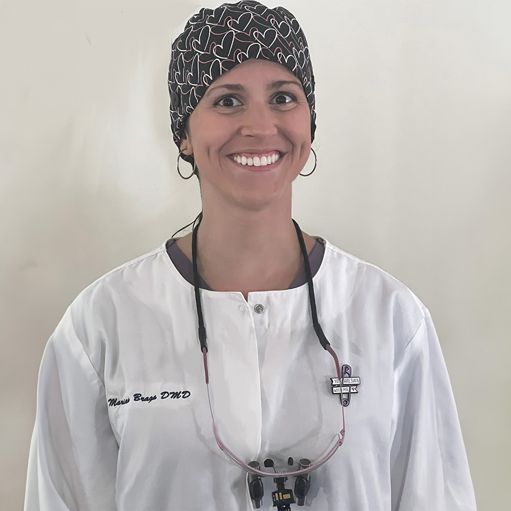 The image shows a person wearing a white lab coat, a headscarf with a floral pattern, and a lanyard around their neck. They are smiling at the camera.