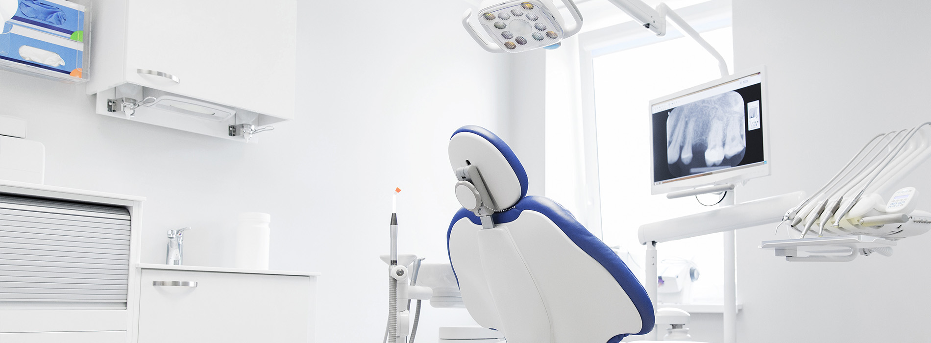 The image shows a modern dental clinic interior with various pieces of equipment, including a dental chair and an X-ray machine.