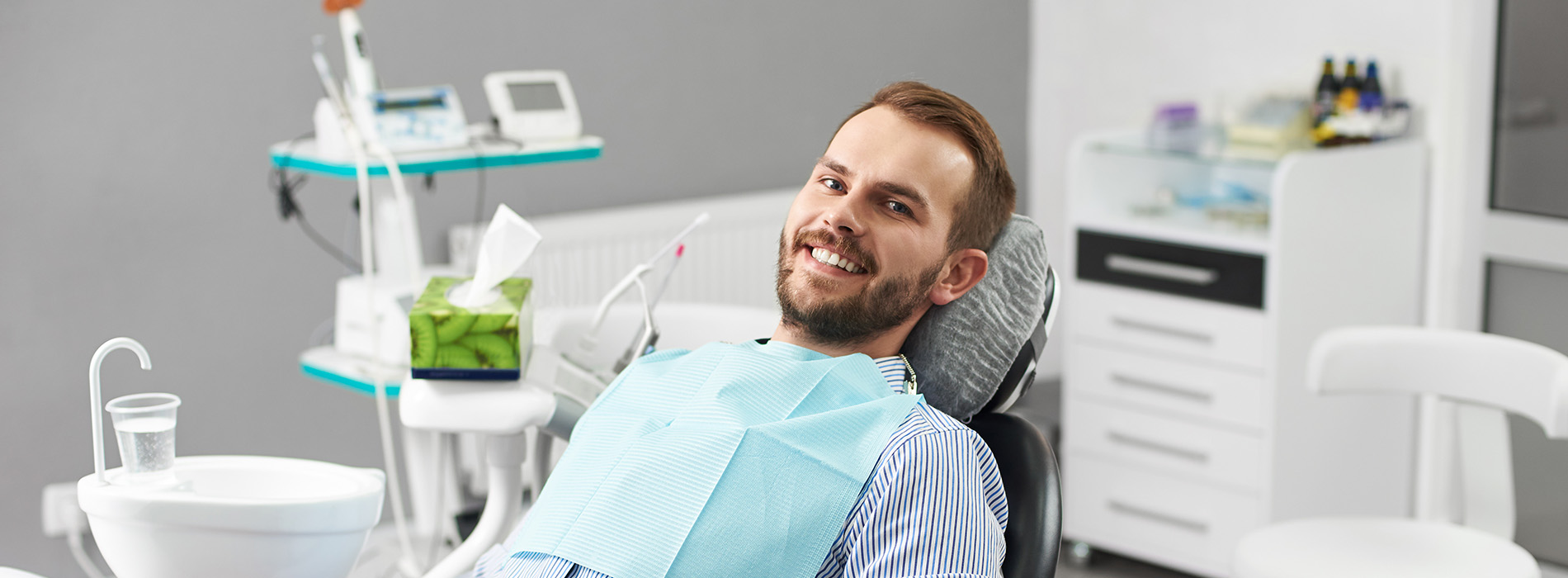 A person is seated in a dental chair, receiving care from a dental professional who stands behind them.