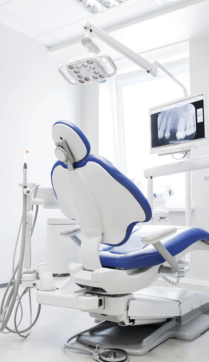 The image shows a modern dental or medical office interior with a dental chair, equipment, and a clean, professional environment.