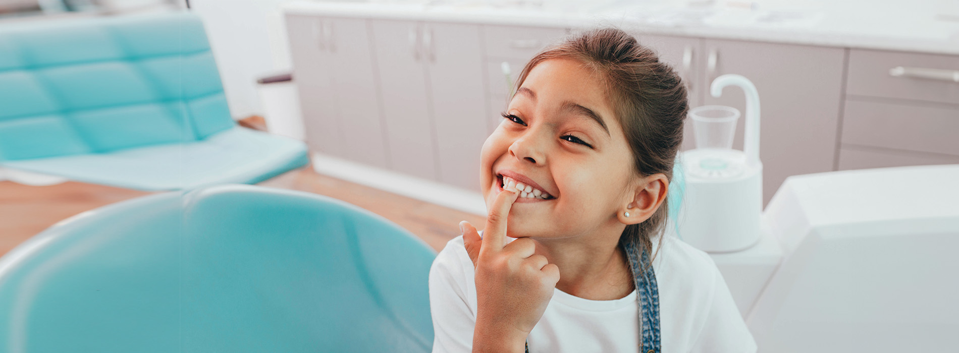 A young girl in a dental office, smiling and pointing at something.