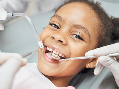 A young girl in a dental chair receiving treatment, with medical professionals attending to her.