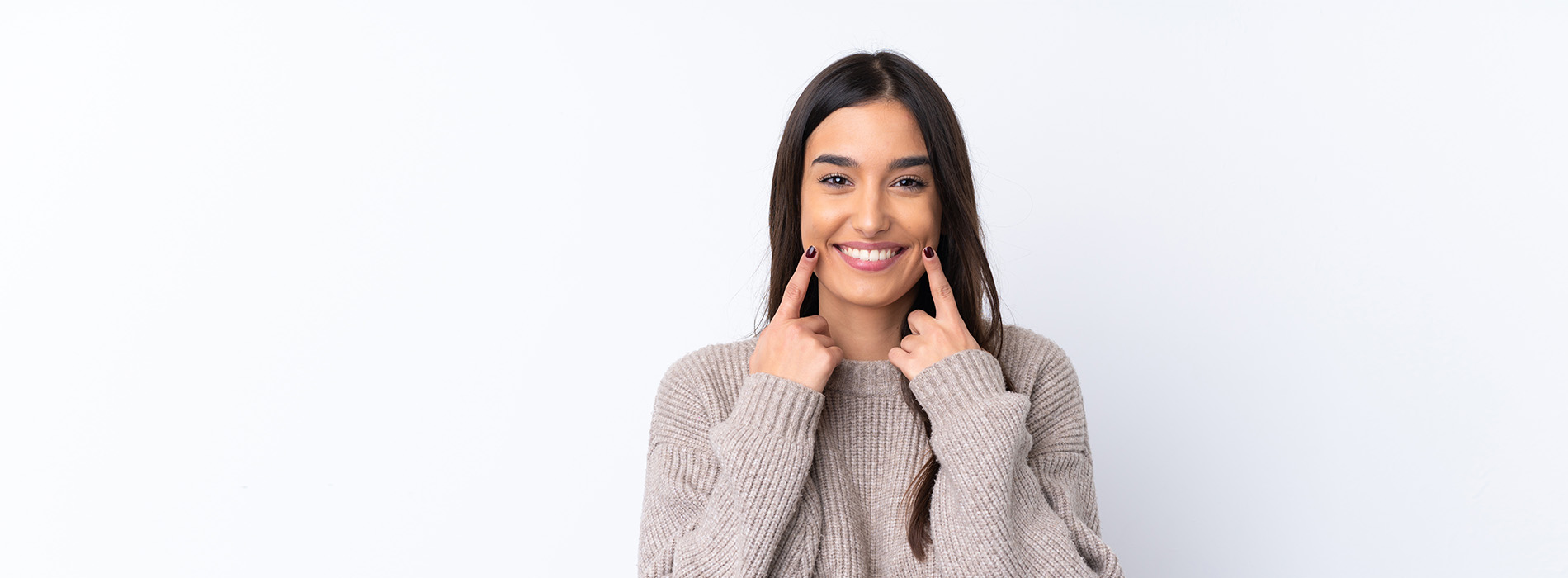 A person is smiling and holding their hand to their face, standing against a white background.