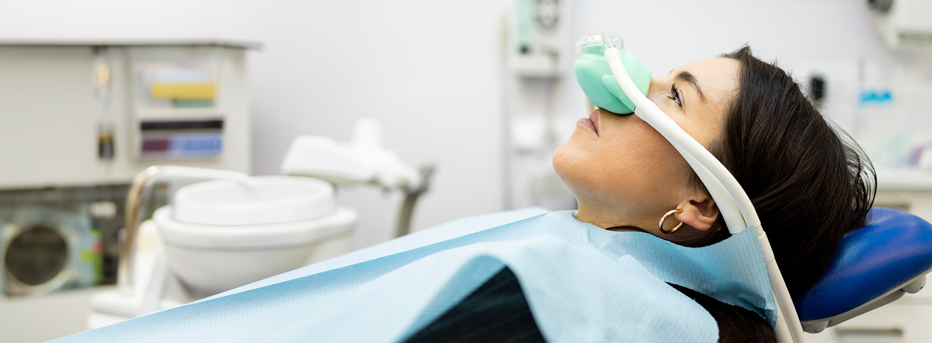 The image shows a person in a dental chair, wearing a face mask and having their teeth cleaned by a dental professional.