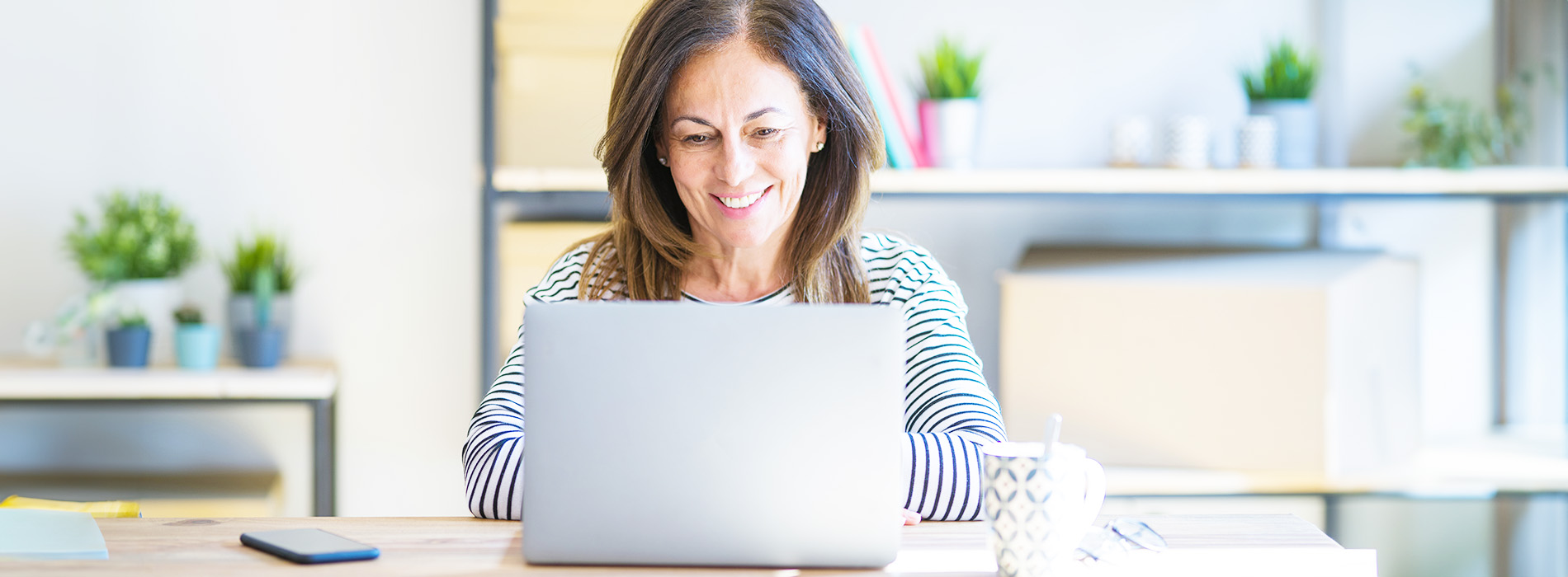 A woman is seated at a desk in an office setting, working on her laptop.