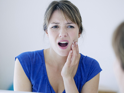 A woman with a surprised expression, looking at her reflection in the mirror while holding her hand to her mouth.